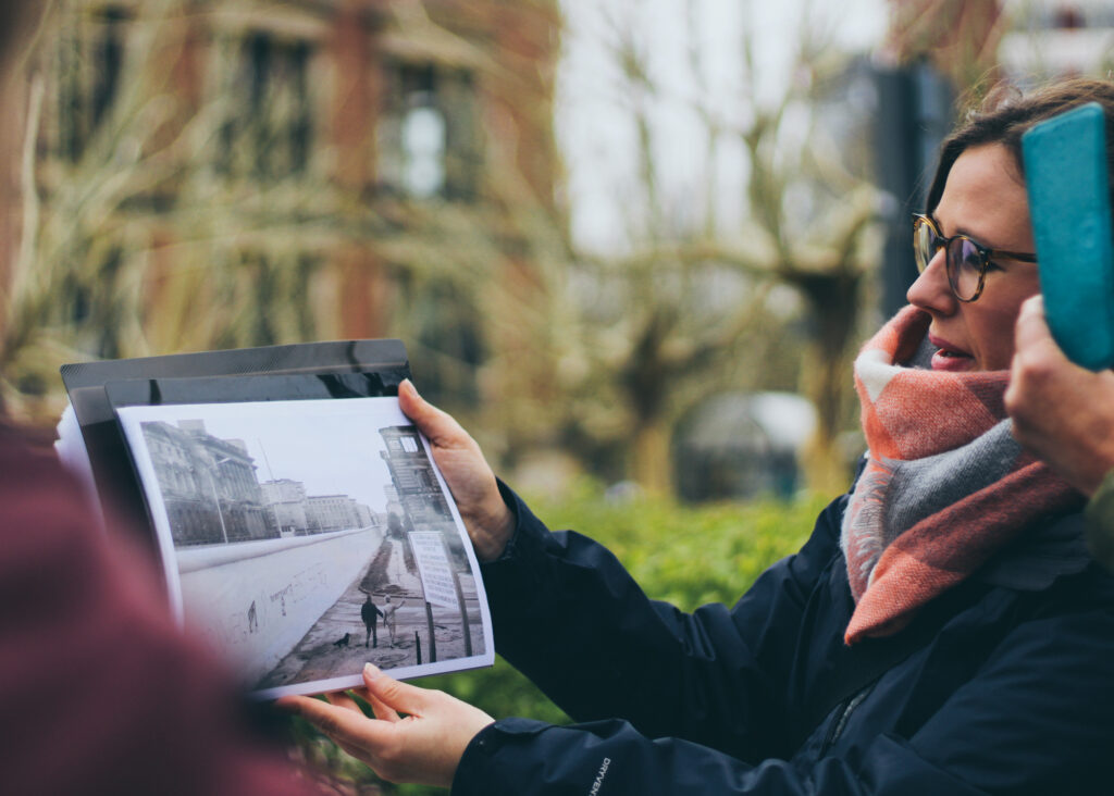 Emma houdt in Berlijn een oude zwart-witfoto van de Muur omhoog, precies waar die stond.